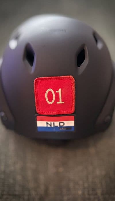 Een zwarte helm met een rode patch met het opschrift “01” en een kleine vlaggenpatch met de letters “NLD”