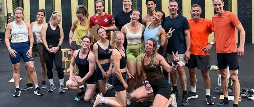 Een groep mensen glimlacht en poseert samen in een CrossFit gym, met sportkleding aan